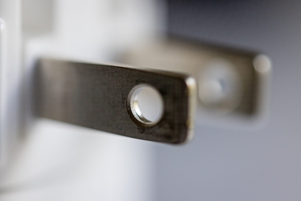 Close-up of the metal prongs of a two-prong electrical plug, with one prong in sharp focus showing a round hole near its tip
