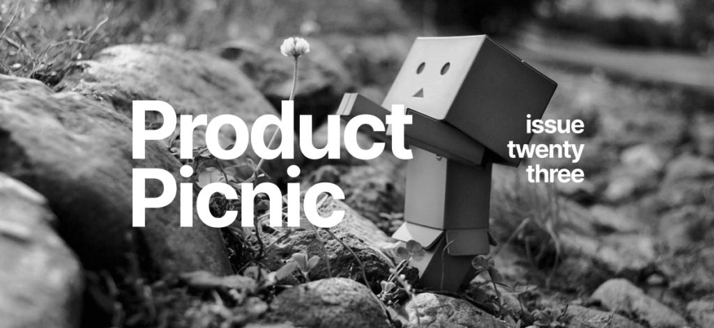 Cardboard robot figure standing among rocks and flowers, reaching toward a single blossom, with the text "Product Picnic issue twenty three" overlaid