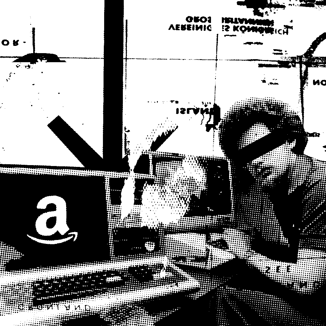 Stylized black-and-white halftone image of a person with eyes obscured, sitting at a desk with an old computer showing the Amazon logo, in front of a cluttered background with partially legible text