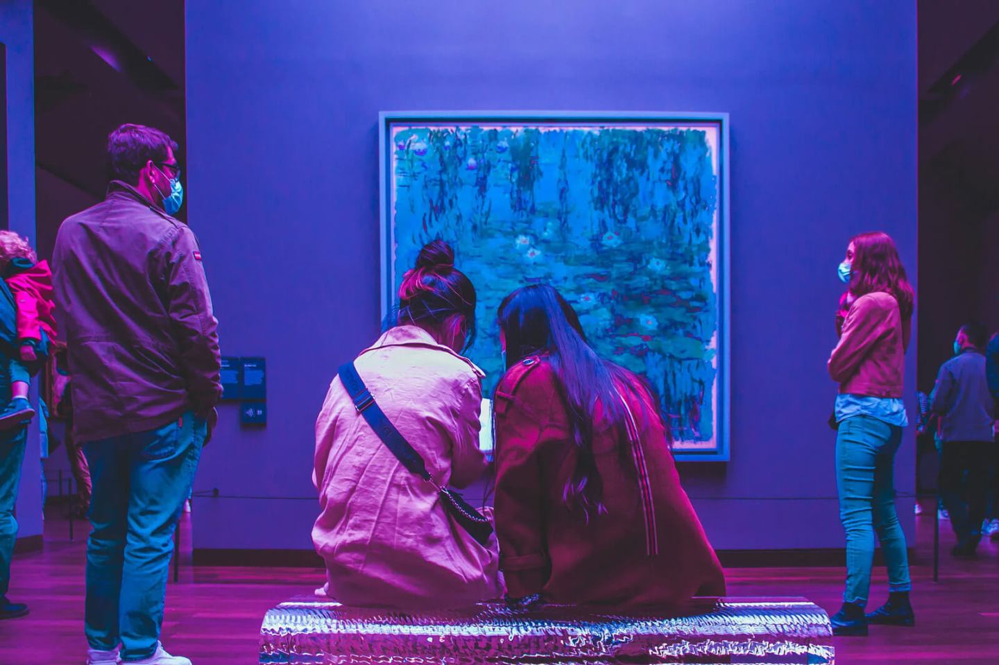 People wearing face masks view an impressionist painting in a museum gallery