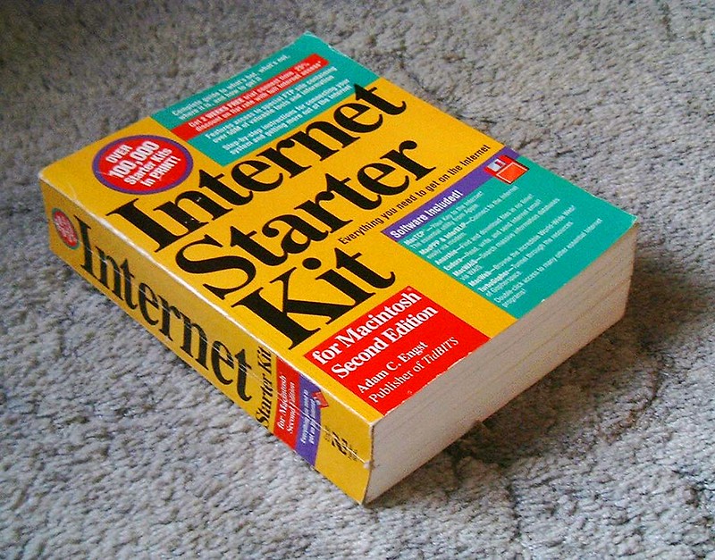 Thick paperback book titled "Internet Starter Kit for Macintosh Second Edition" by Adam C. Engst, featuring a bold yellow cover with red, green, and blue sections, placed on a carpeted floor.
