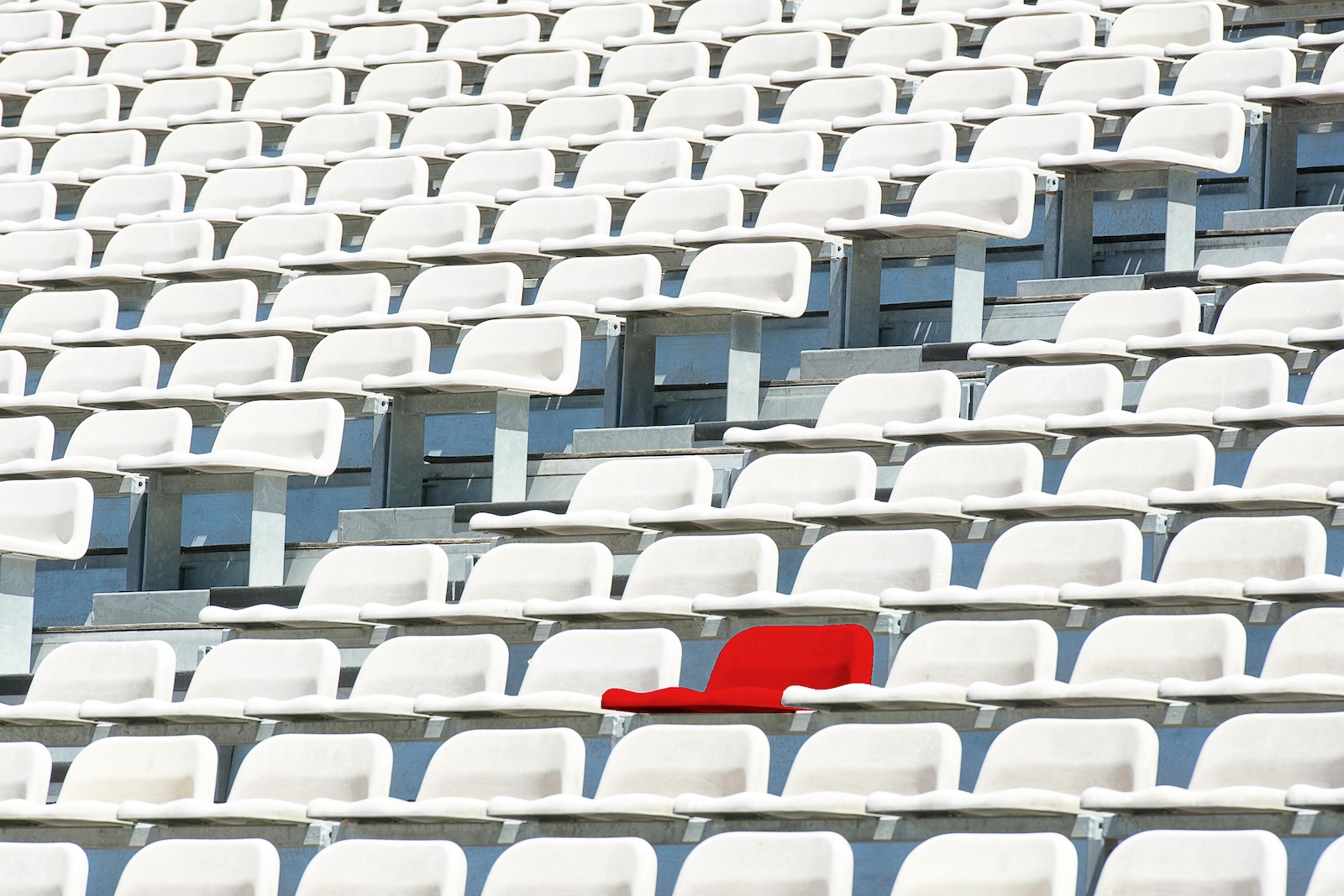 Rows of white stadium seats with one bright red seat standing out in the middle