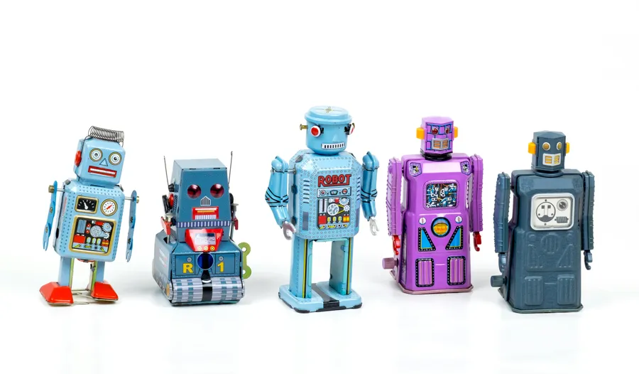 Five colorful vintage-style toy robots with detailed designs and varied expressions, standing side by side on a white back...
